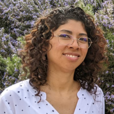 young South American woman with brown curly hair wearing glasses smiling happily wearing a white blouse with black dots